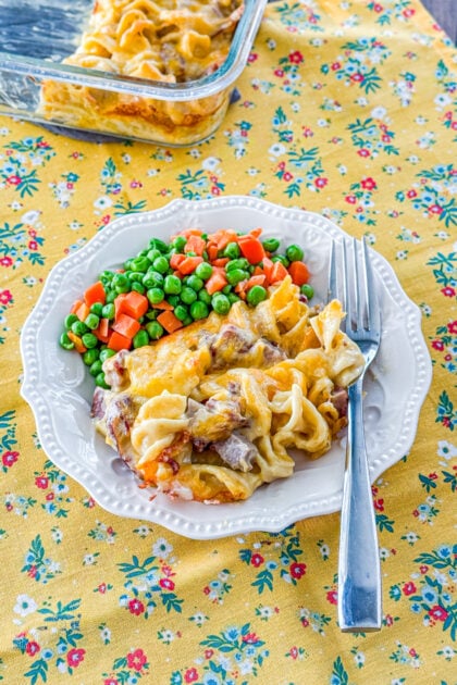 Creamy roast beef noodle casserole on a plate with peas and carrots on the side.