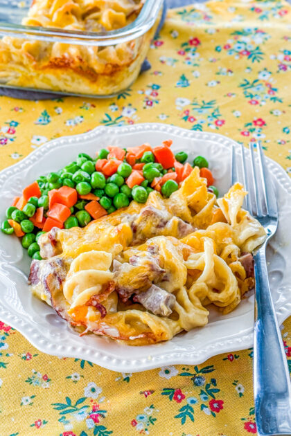 Roast beef casserole served on a plate with a side of peas and carrots.