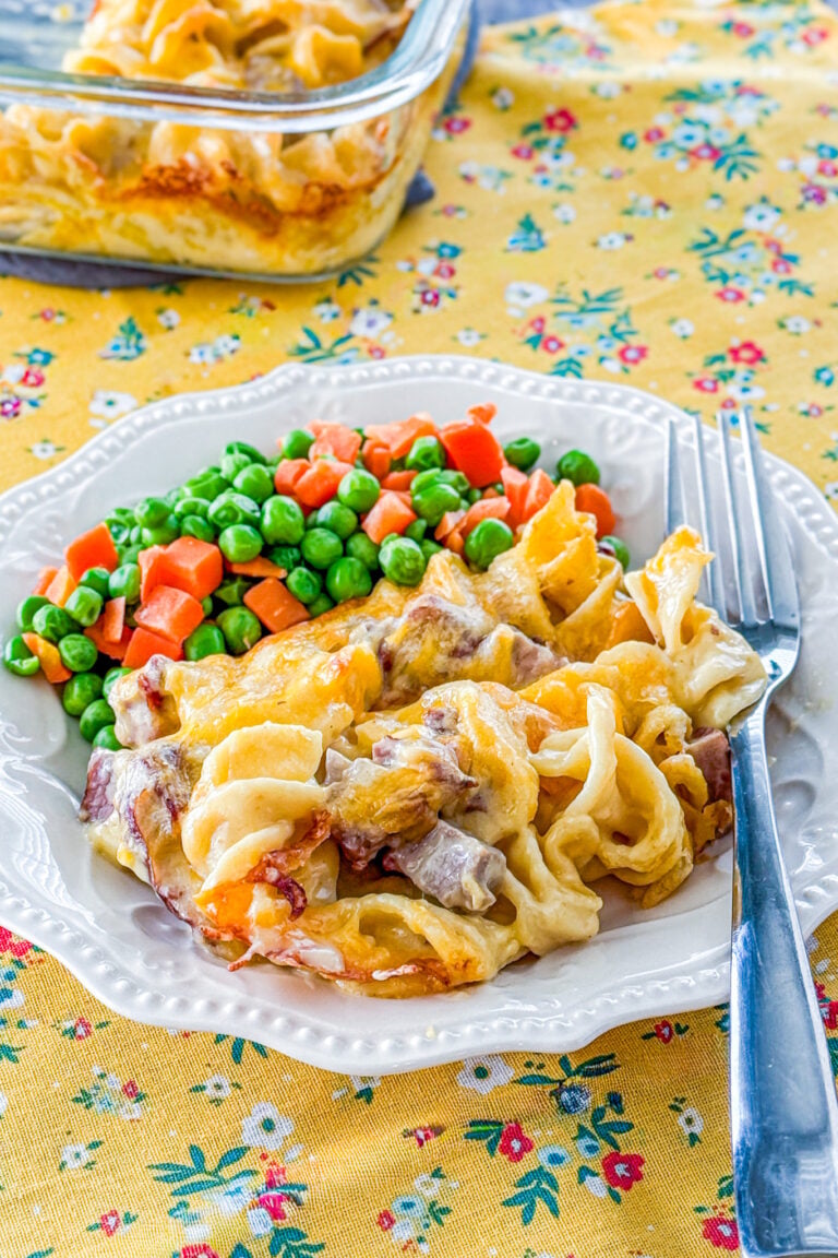 Roast beef casserole served on a plate with a side of peas and carrots.