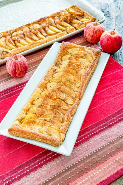 Golden puff pastry apple tart topped with overlapping apple slices on serving platter