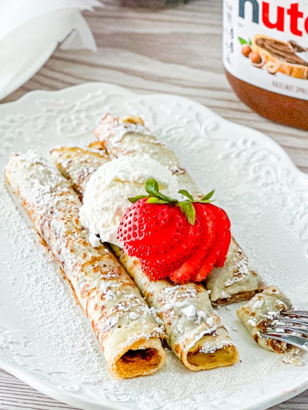 3 nutella crepes on a white plate srinkled with powdered sugar