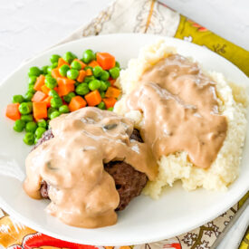 Stuffed beef patty on a plate fith mashed potatoes and peas/carrots
