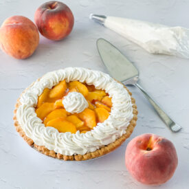 a whole best fresh peach pie with fresh peaches around it and pie server