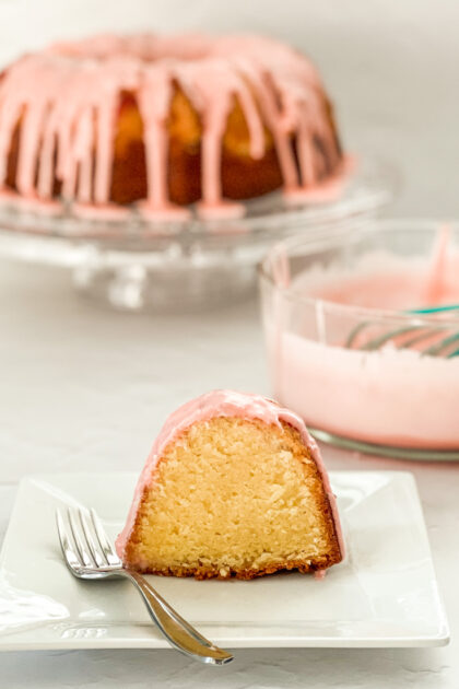 Shirley Temple Bundt Cake on a plate with bowl of frosting in the background.