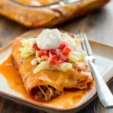 easy ground beef enchiladas topped with lettuce, salsa, and sour cream