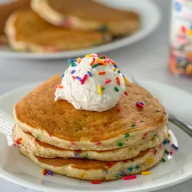 birthday cake pancakes topped with whipped cream and sprinkles