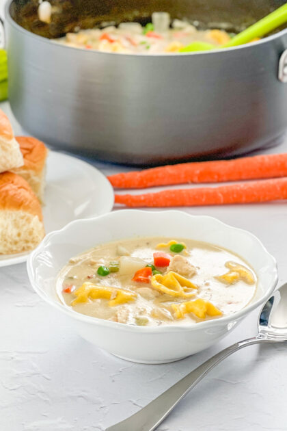 Creamy Chicken Tortellini Soup in a white bowl with pot of soup in background
