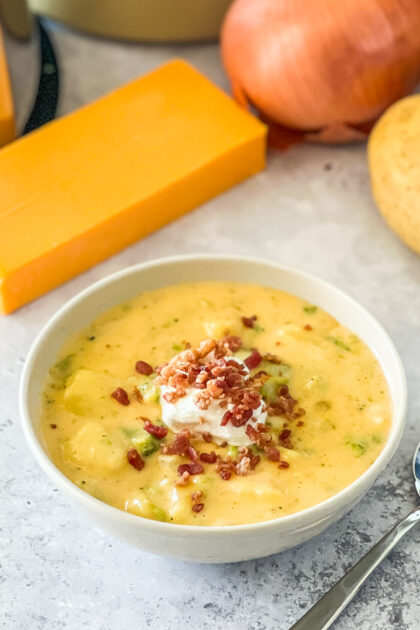 bowl of super loaded baked potato soup with cheese and potatoes in background