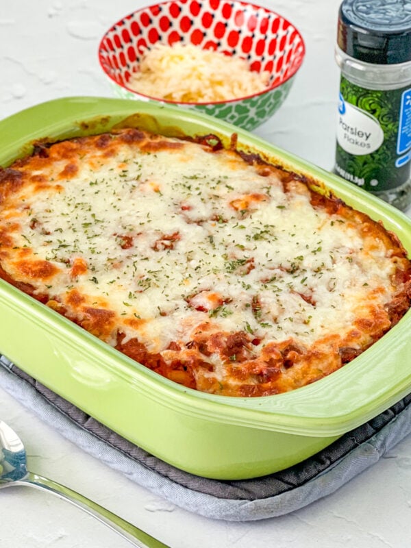 Italian ground beef casserole in a light green baking pan with cheese and pasley in background