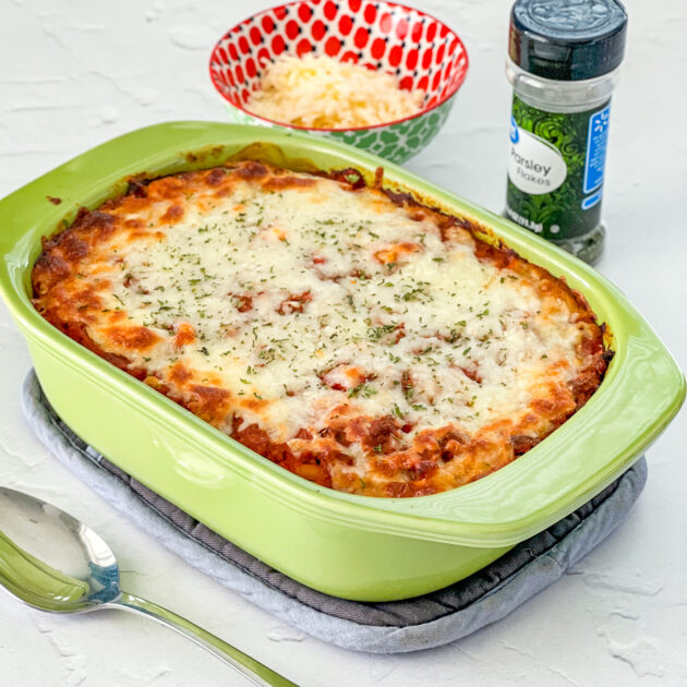 Italian ground beef casserole in a light green baking pan with cheese and pasley in background