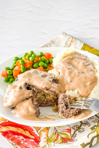 Beef stuffed patty cut open with mashed potatoes and peas/carrots