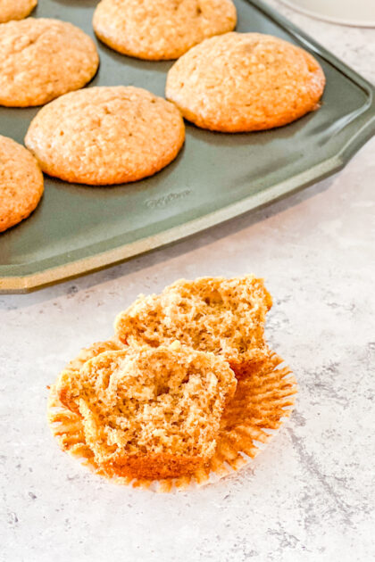 cinnamon banana muffin broken in half with full muffins in tin in the background