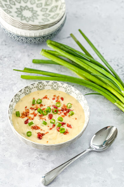 bowl of cheesy wild rice soup by a bunch of green onions