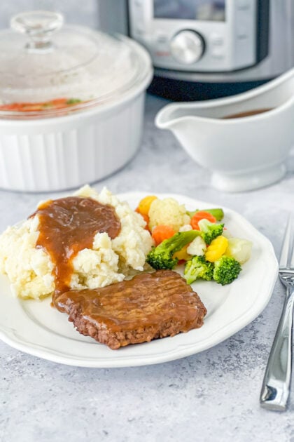 Instant Pot Cubed Steak with Gravy on a white plate paired with mashed potatoes and steamed vegetables