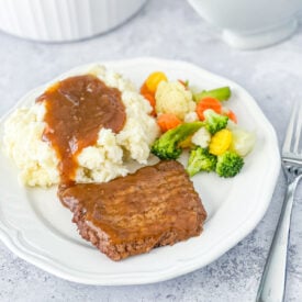Instant Pot Cubed Steak with Gravy on a white plate with mashed potatoes and steamed vegetables