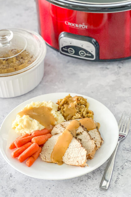 Slices of slow cooker savory turkey breast on a white plate with crock pot in background