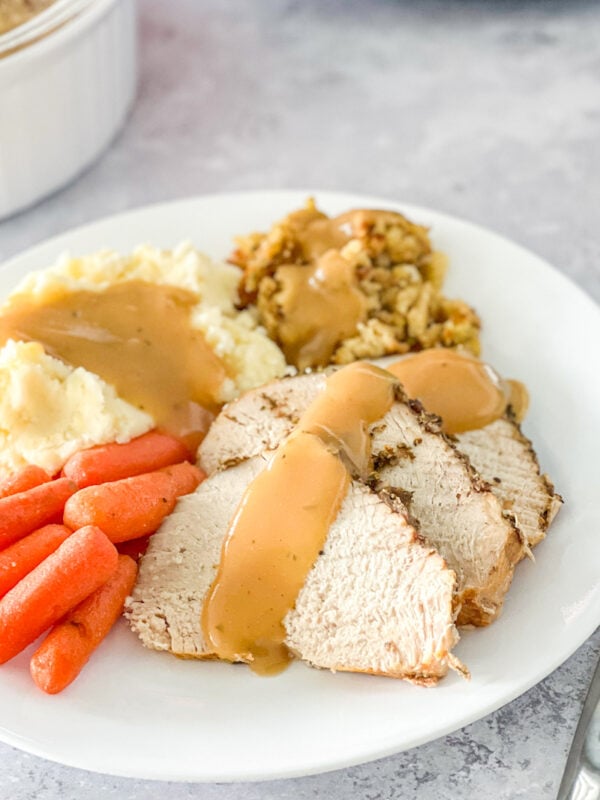 Slices of slow cooker turkey breast served with stuffing, mashed potatoes, and carrots