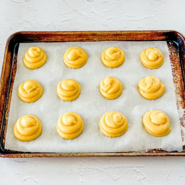 piped cream puffs on a baking sheet lined with parchment