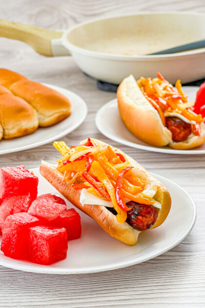 philly cheesesteak hot dog on a white plate wuth watermelon