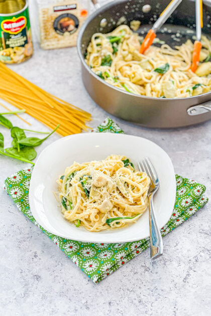 bowl of cream spinach artichoke pasta with ingredients in backgound
