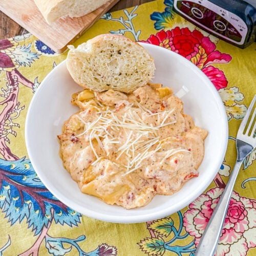 Slow Cooker Marry Me Chicken Tortellini in a white bowl on a flower table cloth