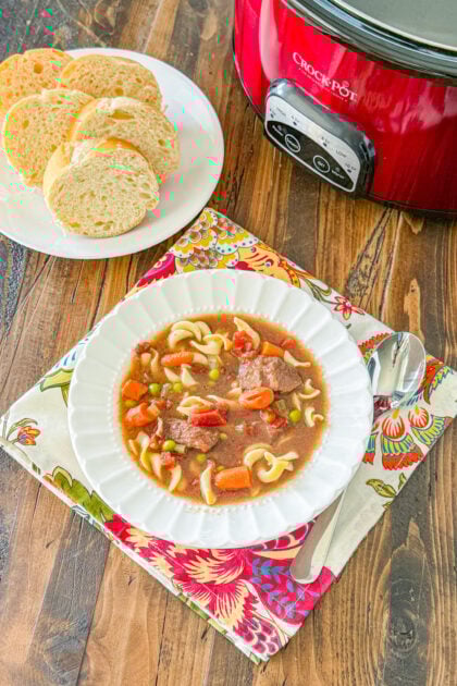 slow cooked vegetable beef noodle soup ina white bowl with a side of French bread