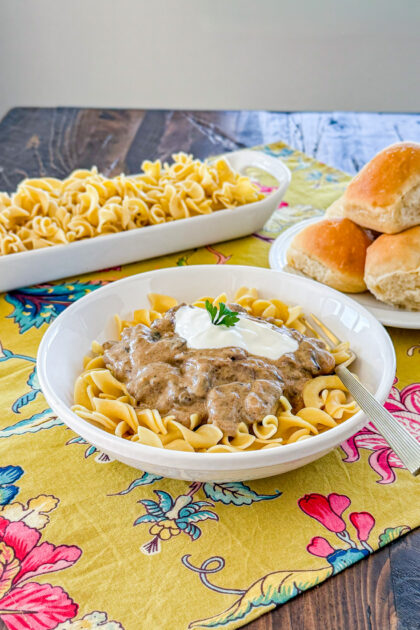 bowl of egg noodles tops with instant pot mushroom beef stroganoff sauce, a dollop of sour cream, and chopped green onion