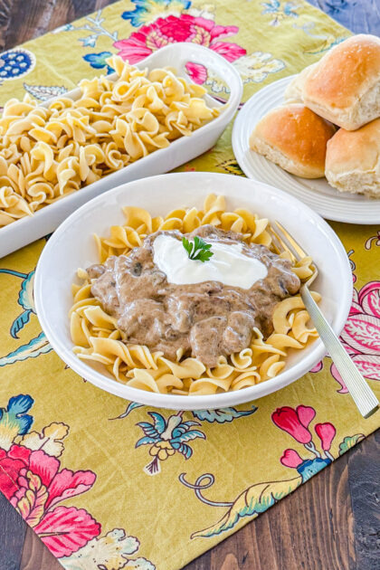 bowl of egg noodles tops with mushroom beef stroganoff sauce, a dollop of sour cream, and chopped green onion