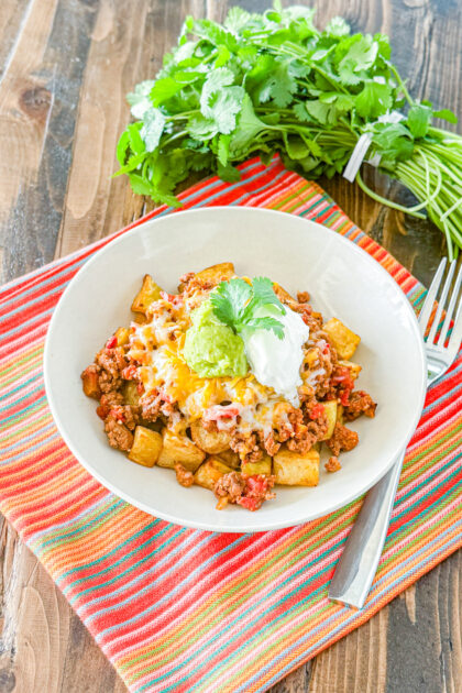 a bunch of cilantro next to a loaded potato taco bowl
