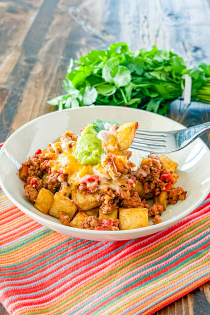 bowl with roasted potato, taco meat, cheese, guacamole and sour cream with a bite of the bowl on a fork