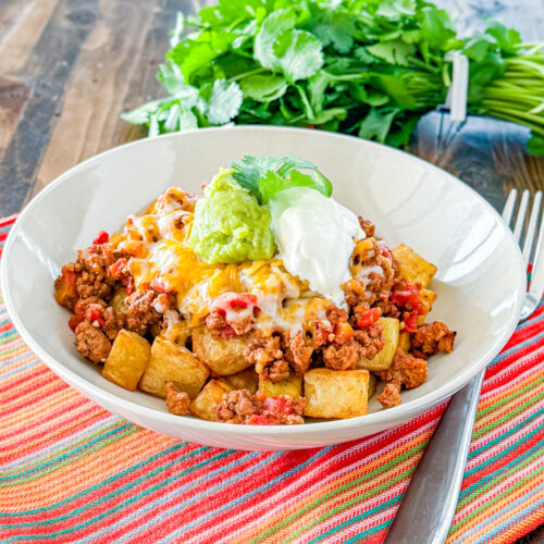 bowl filled with a layer of roasted potatoes followed with taco meat, shredded cheese, guacamole, and sour cream