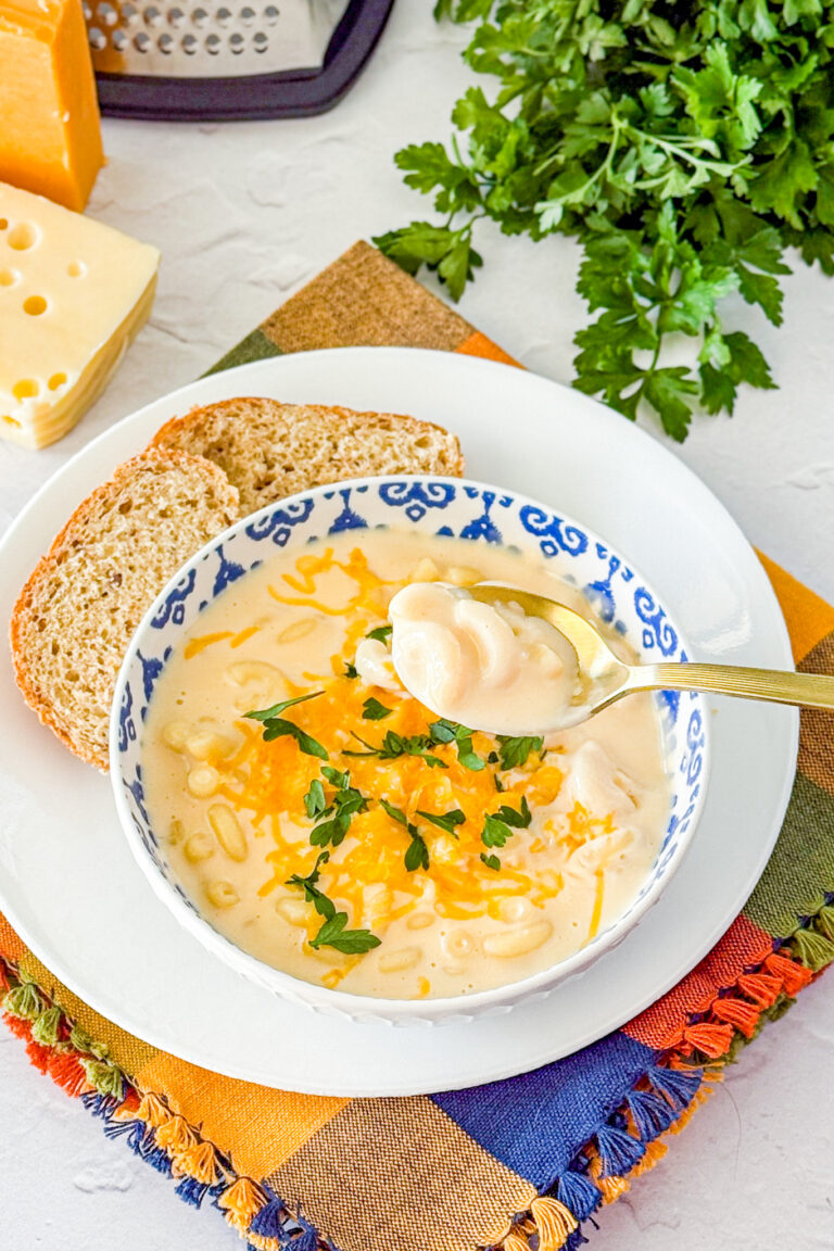 easy mac and cheese soup in a blue and white bowl with bread on the side