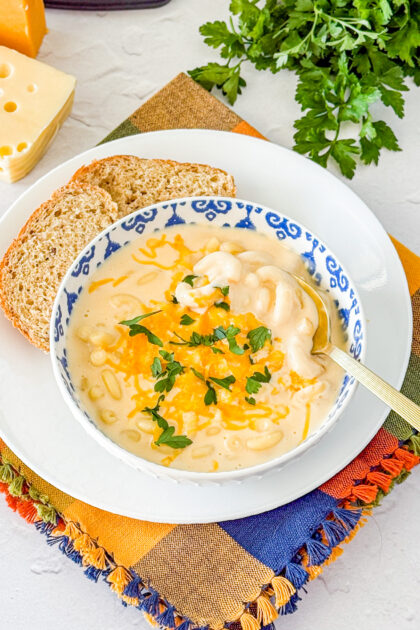mac and cheese soup recipe in a blue and wite bowl with bread on the side