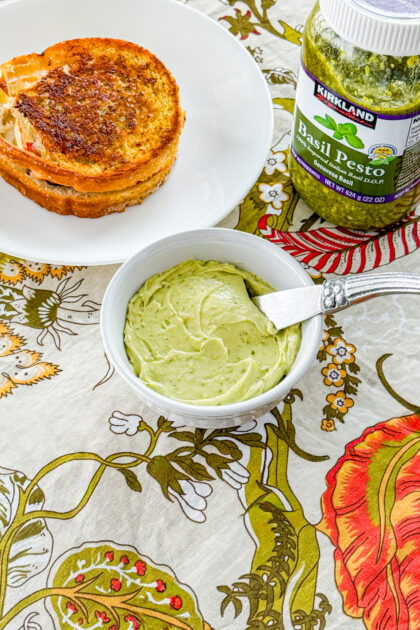 small white bowl with pesto butter inside and a knife to spread it with