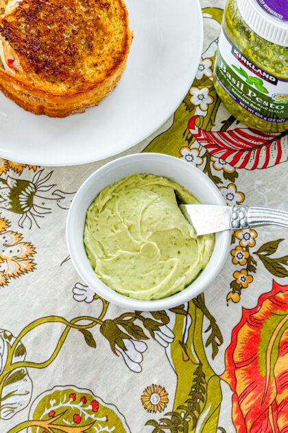 a bowl of pest butter next to a grilled cheese sandwich and a bottle of basil pest0