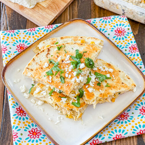 wedsges of chicken and corn quesadilla on a cream plate sprinkle with extra cotija cheese and cilantro