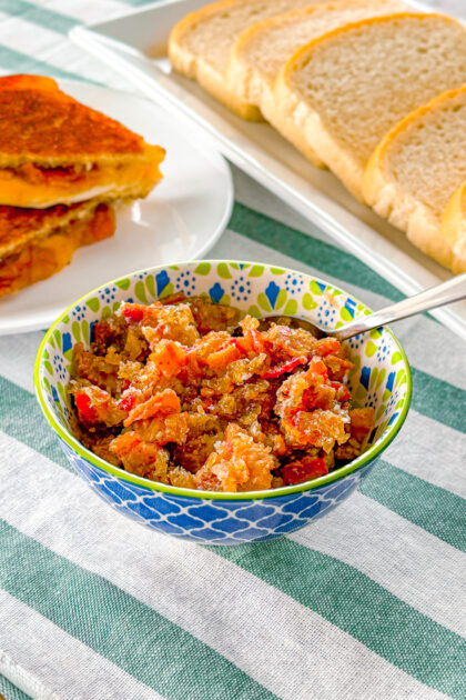 bacon jam in a bowl with slices of bread and a grilled cheese sandwich in the background