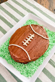 homemade chocolate cake shaped like a football surrounded by green colored coconut