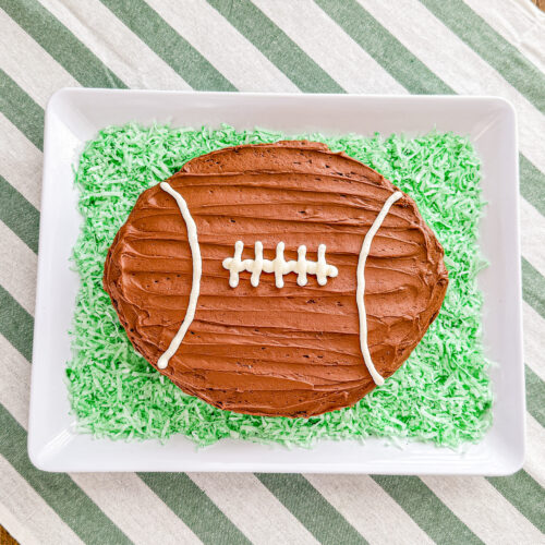 football shaped chocolate cake on a white tray surrounded with green colored shredded coconut