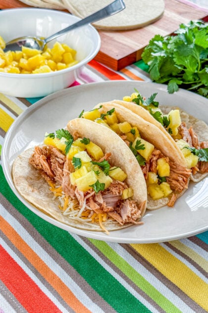 Slow cooker tacos al pastor topped with fresh pineapple, cilantro, and lime