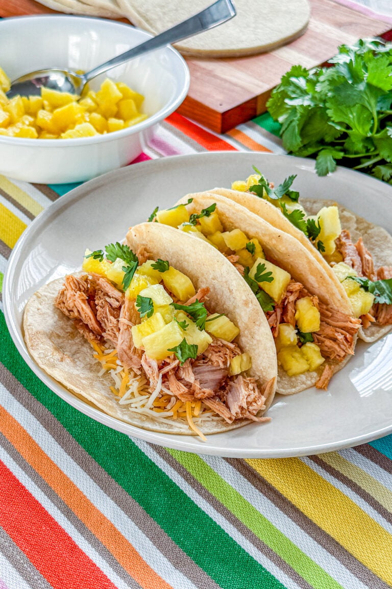 Slow cooker tacos al pastor topped with fresh pineapple, cilantro, and lime
