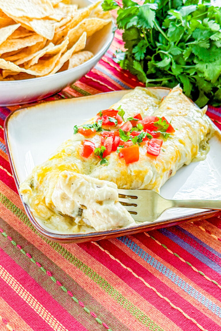 Creamy green chile chicken enchiladas topped with melted cheese, tomatoes, and cilantro
