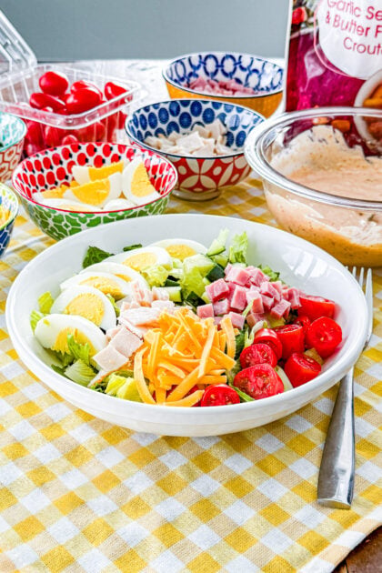 Chef salad with sliced hard-boiled eggs, ham, turkey, and cheddar cheese over romaine