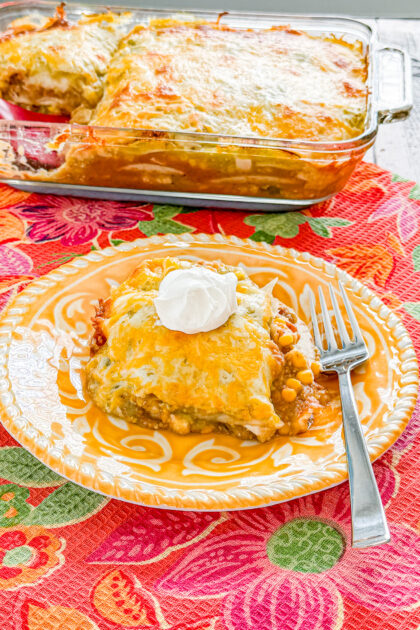 Chicken taco casserole with chicken, refried beans, corn, green salsa, tortillas, and melted cheese