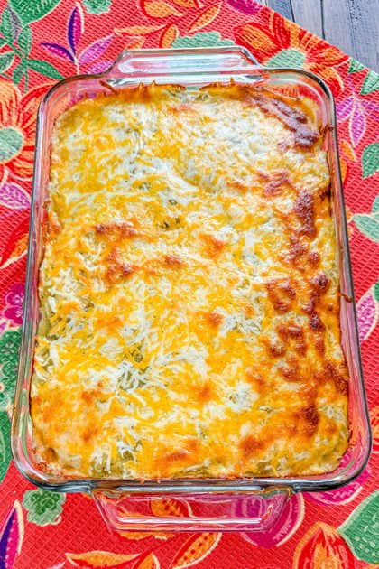 Layered chicken taco casserole topped with green salsa and shredded cheese after baking