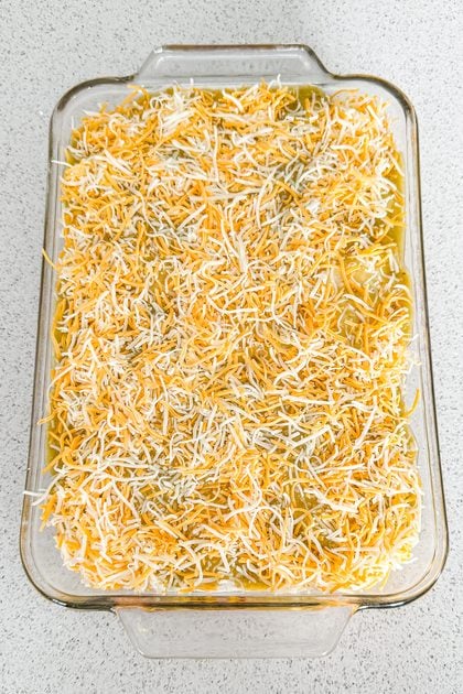 Layered chicken taco casserole topped with green salsa and shredded cheese before baking