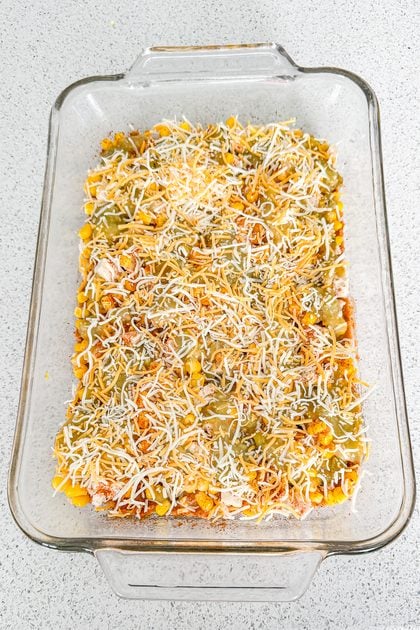 Chicken taco casserole being layered with tortillas, refried beans, chicken, corn, green chilies, and cheese