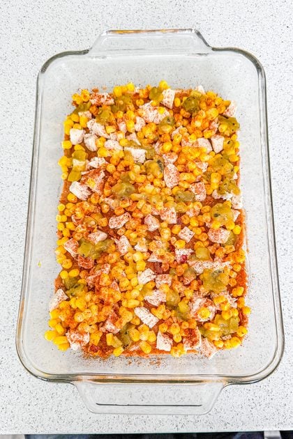 Chicken taco casserole being layered with first layer of tortillas, refried beans, chicken, corn, and green chilies