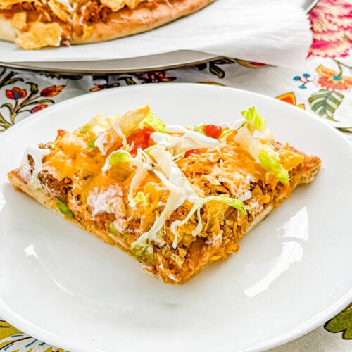 Slice of loaded taco pizza with ground beef, beans, cheese, lettuce, and sour cream