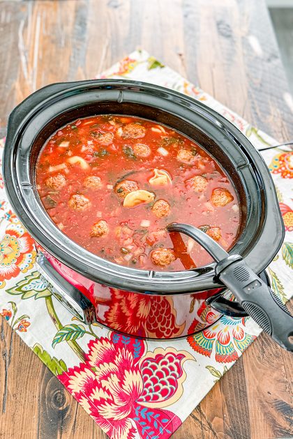 Meatball tortellini soup in a slow cooker with tomatoes, spinach, carrots, and Italian meatballs